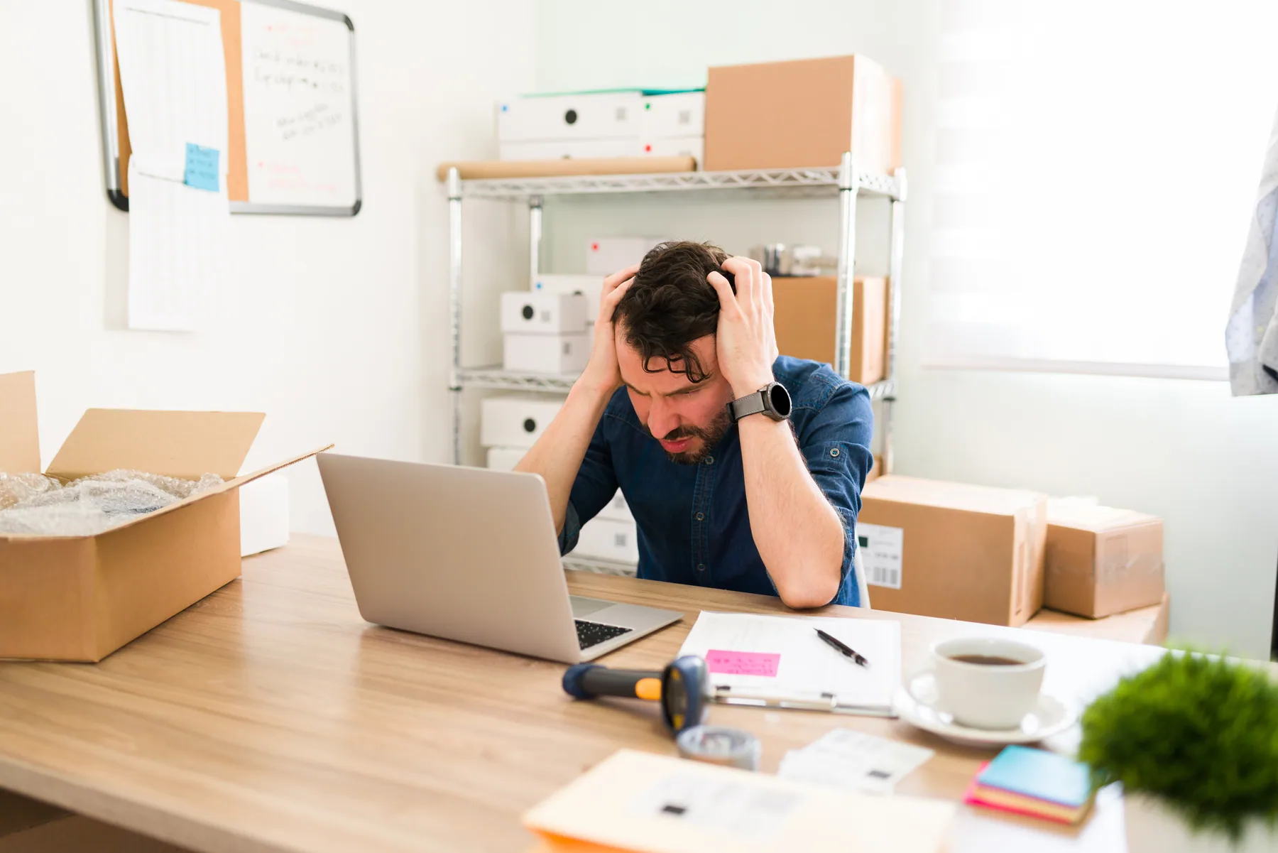 A seller with his head in his hands at a desk stacked with boxes